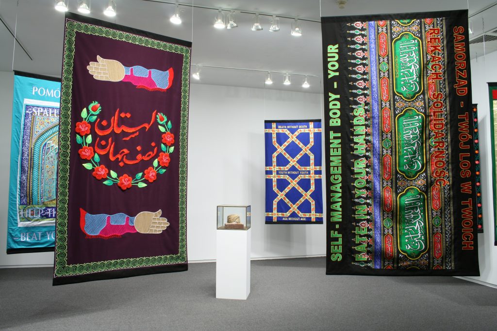 Wheat Molla, 2011, wheat, cotton, glue, brick, 45 x 35 x 25 cm, Friendship of Nations, 2011, banners, embroidered fabric, silkscreen, 200 x 120 cm, courtesy the Third Line Gallery, Dubai and Kraupa-Tuskany Zeidler Galerie, Berlin